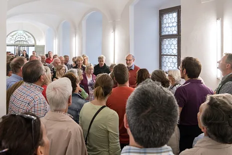Wolfgang Hopfgartner, Heimatpfleger der Stadt Burghausen, umringt von Besucherinnen und Besuchern bei einer Führung durch das Akademiezentrum