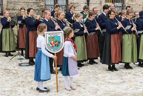 Zwei Mädchen halten das Banner der Musikkapelle St. Georg Mehring-Raitenhaslach, im Hintergrund die Musikerinnen und Musiker
